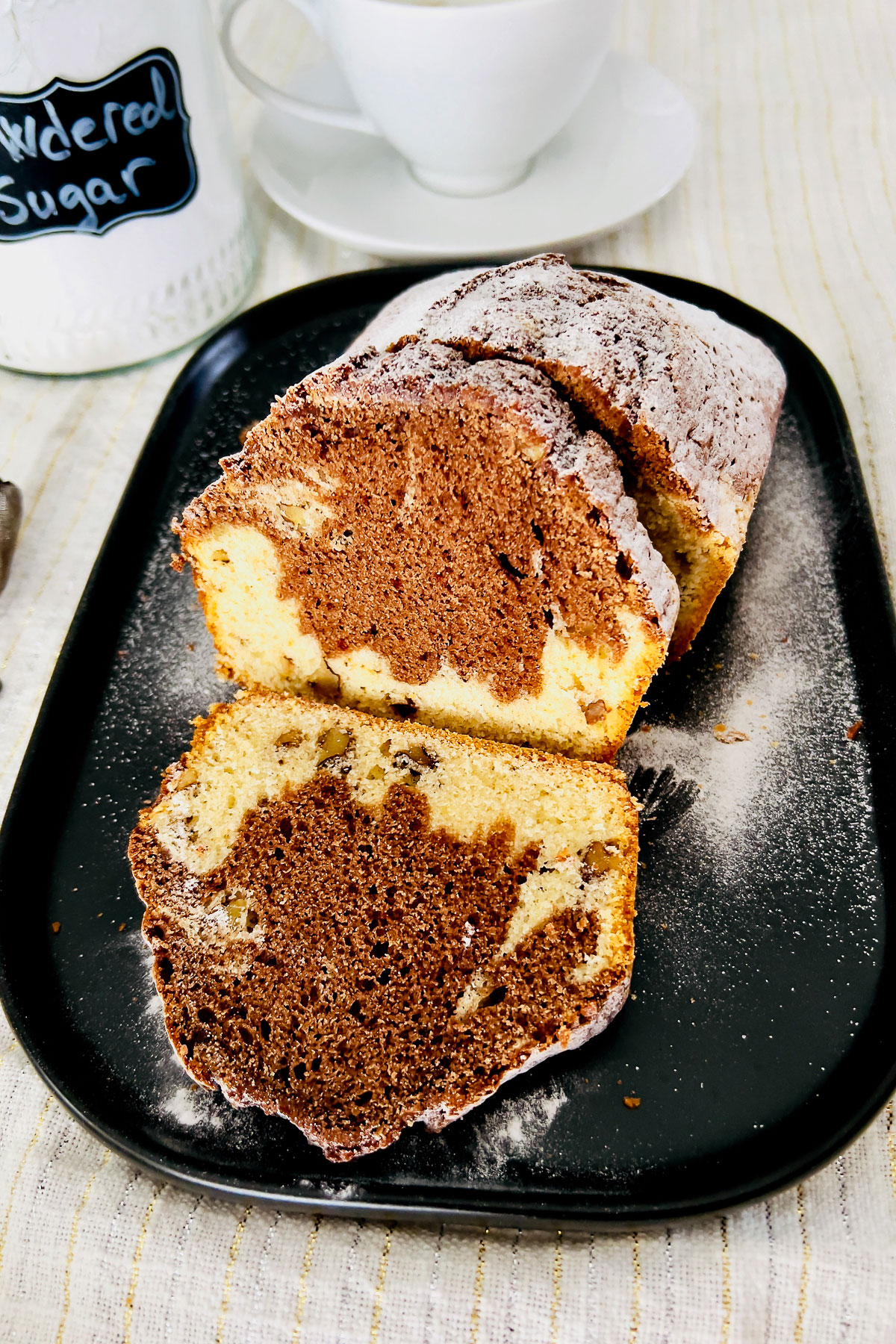 Marble pound cake on black platter with coffee cup.