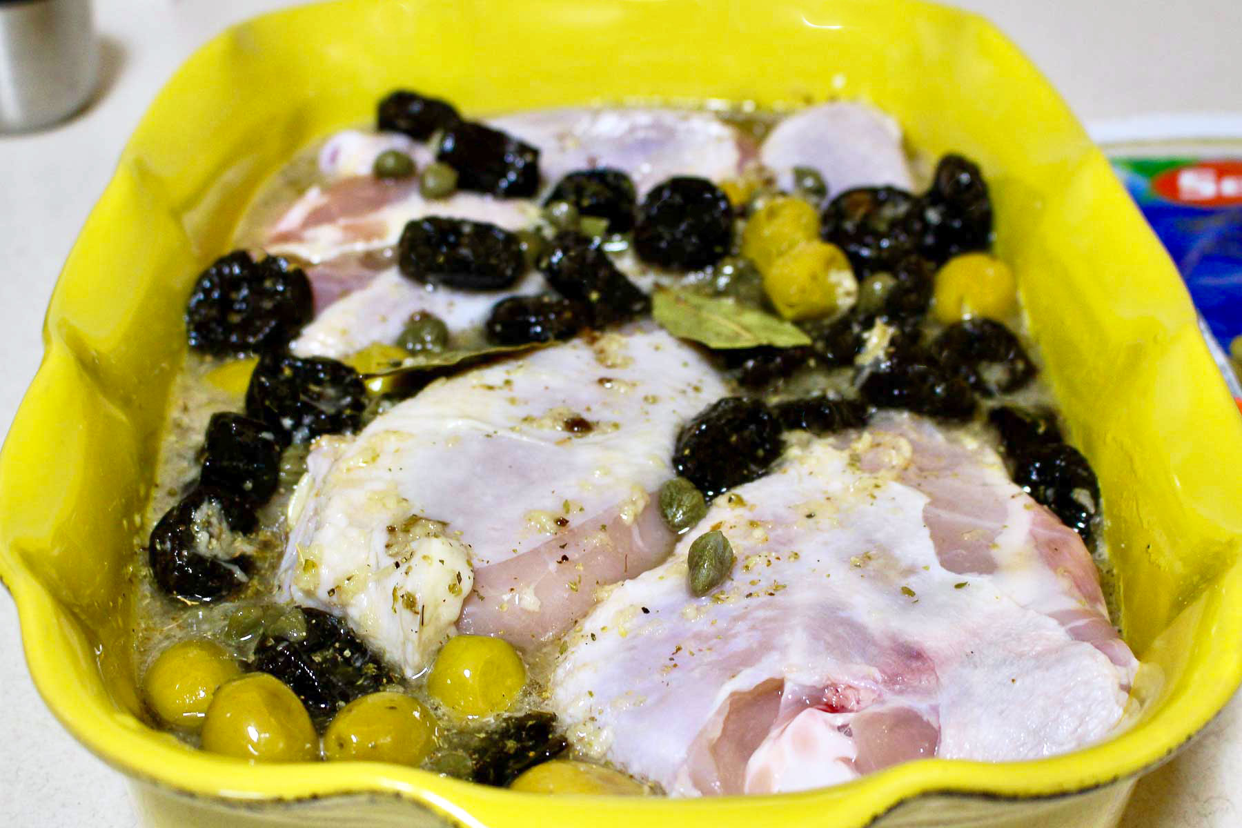 Marinating unbaked Chicken Marbella in a yellow baking dish.