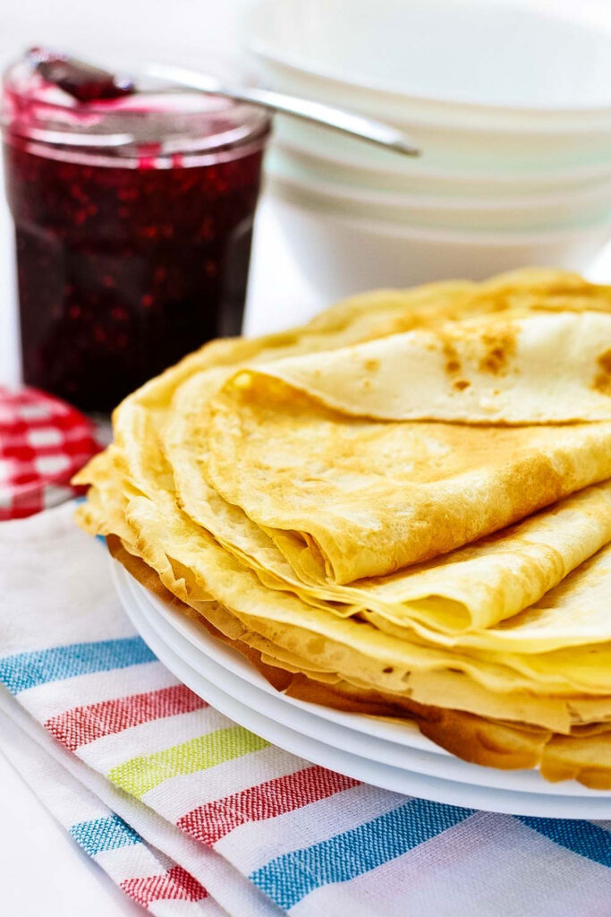 Crepes with a jar of raspberry jam in the background0