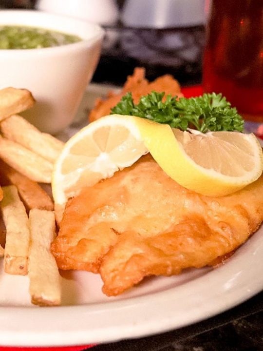 Fried fish on a plate served with lemon wedges and French Fries