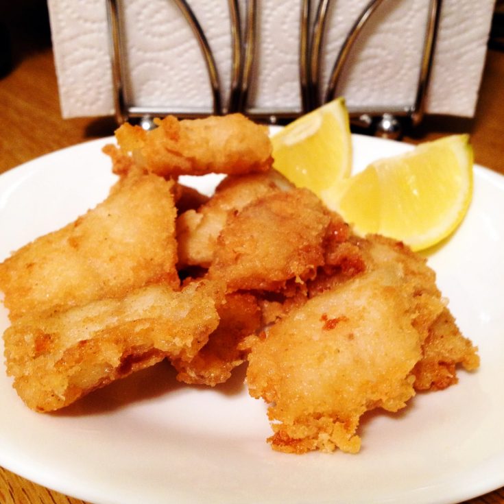 Fried fish on a plate served with lemon wedges