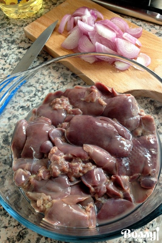Raw Chicken Livers in aglass bowl with red onion chopped in the background