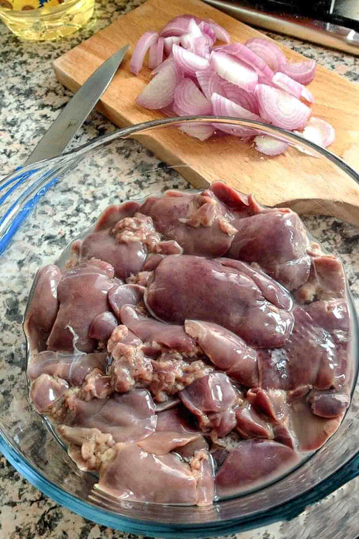 Chicken livers in a bowl and red onions in the background.