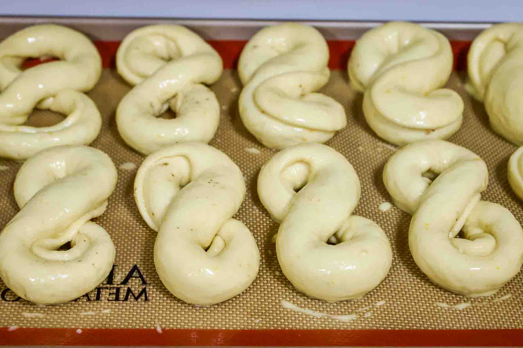 Unbaked mucenici on the baking sheet brushed with egg.