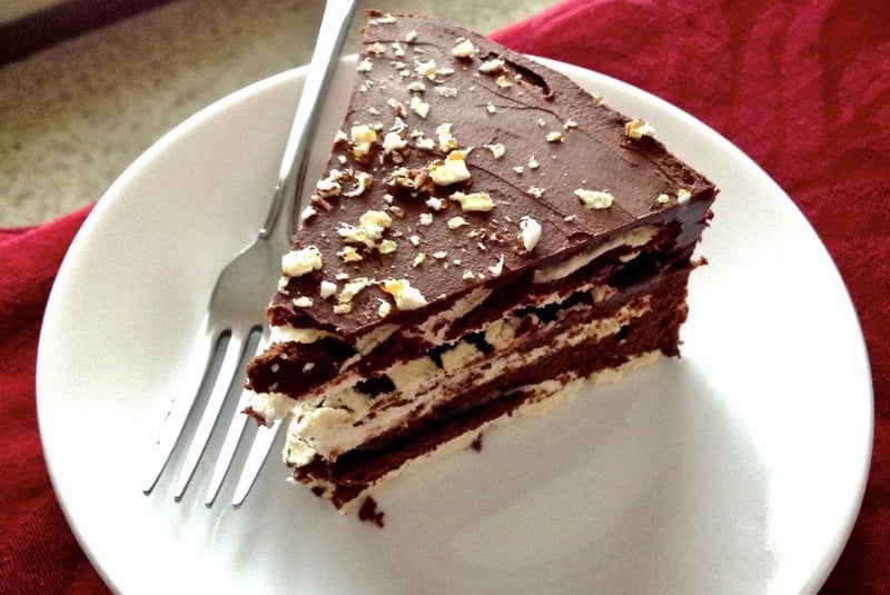 This is a classic European chocolate ganache meringue torte recipe. Easy to make but decadent, this recipe is the perfect option for the chocolate lovers. Classic European chocolate ganache meringue torte- slice of cake on white plate with fork