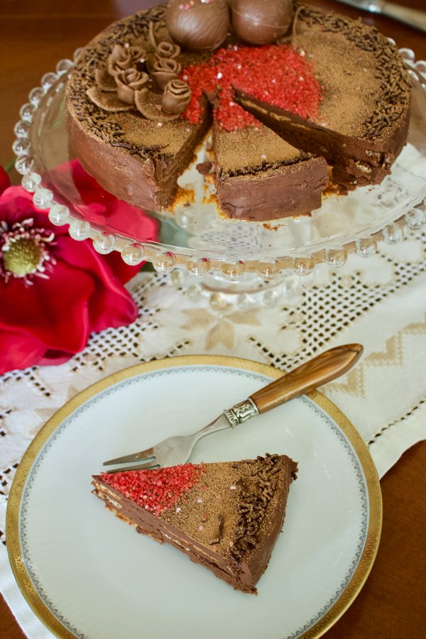 This is a classic European chocolate ganache meringue torte recipe. Easy to make but decadent, this recipe is the perfect option for the chocolate lovers. Classic European chocolate ganache meringue torte- slice of cake on a white plate with fork . Cake sitting on a cake platter in the background- overhead picture