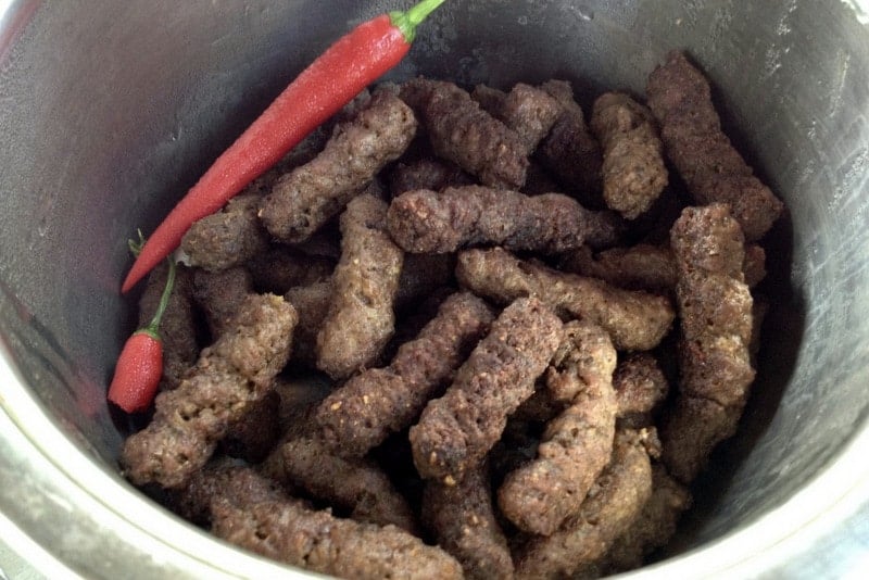 Mititei- Romanian Grilled Sausages are made with ground beef, garlic and other spices. They are served with mustard, bread, and cold beer. Mititei- Romanian Grilled Sausages in a bowl with hot red pepper