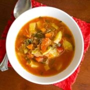 Tomato And Zucchini Soup in a white bowl with spoon.