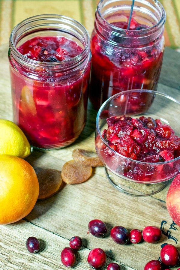 picture of oranges, dried apricots, cranberries next to chutney sitting on a wooden board