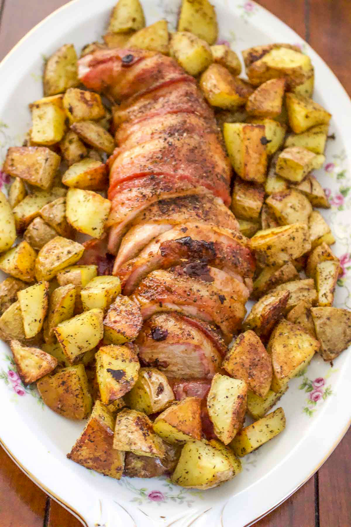 Pork Tenderloin wrapped in Bacon with roasted potatoes on a serving tray.