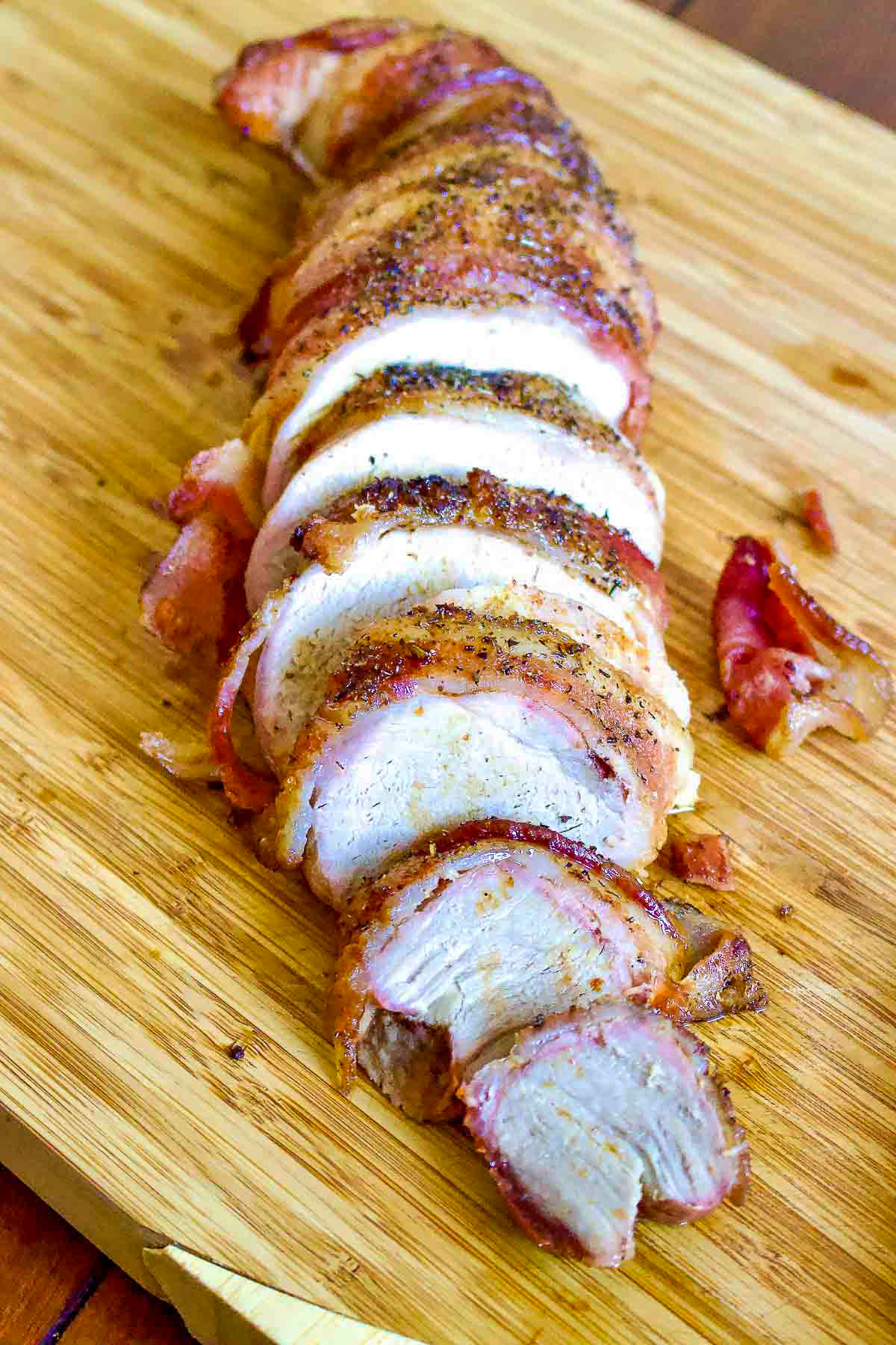 Roasted Pork wrapped in bacon on cutting board.