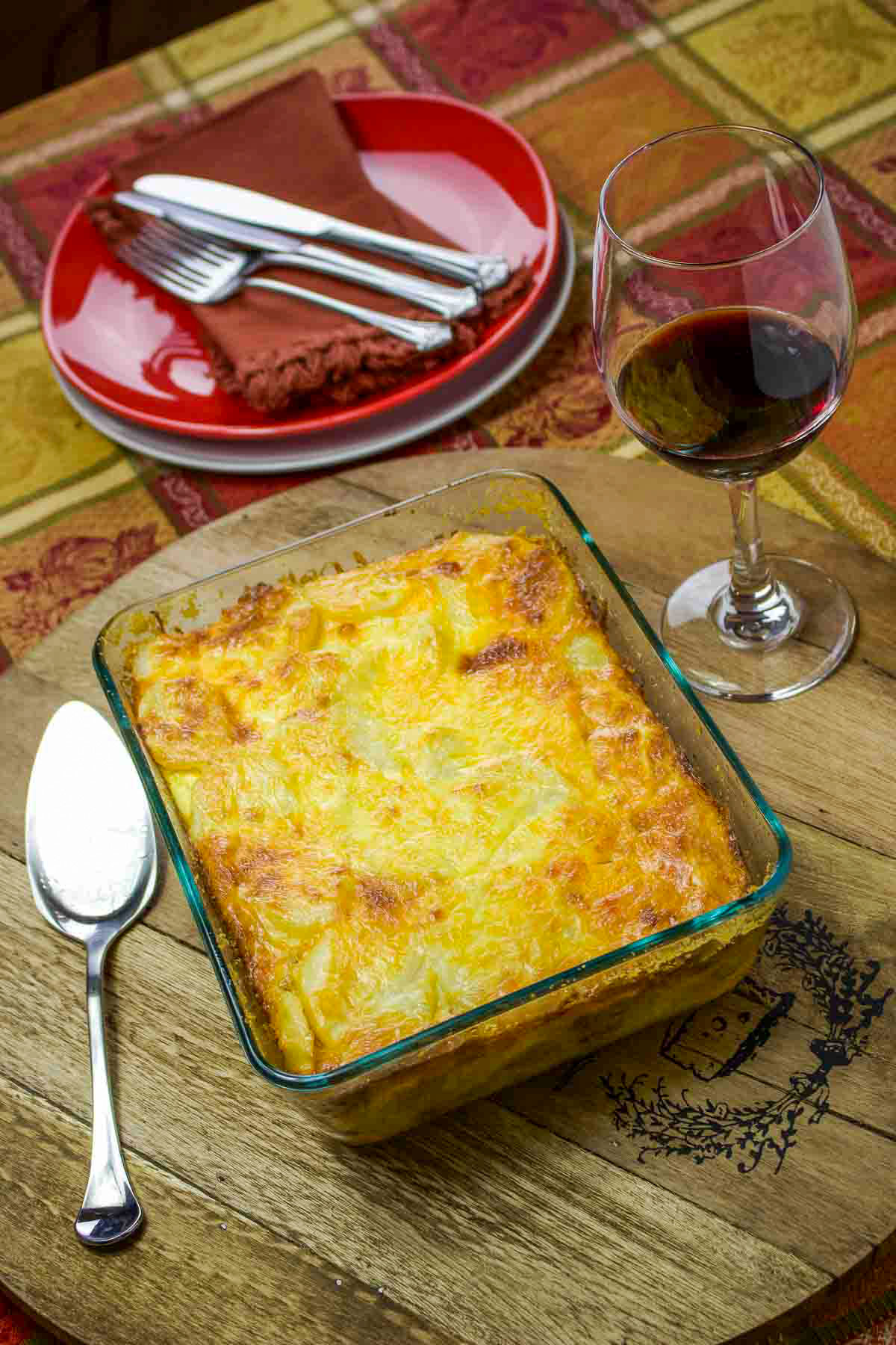 The Romanian Authentic Potato Moussaka is made with layers of potatoes and minced meat. This dish is comfort food, perfect for a family! Potato Moussaka on baking pan with wine and plates for dinner.