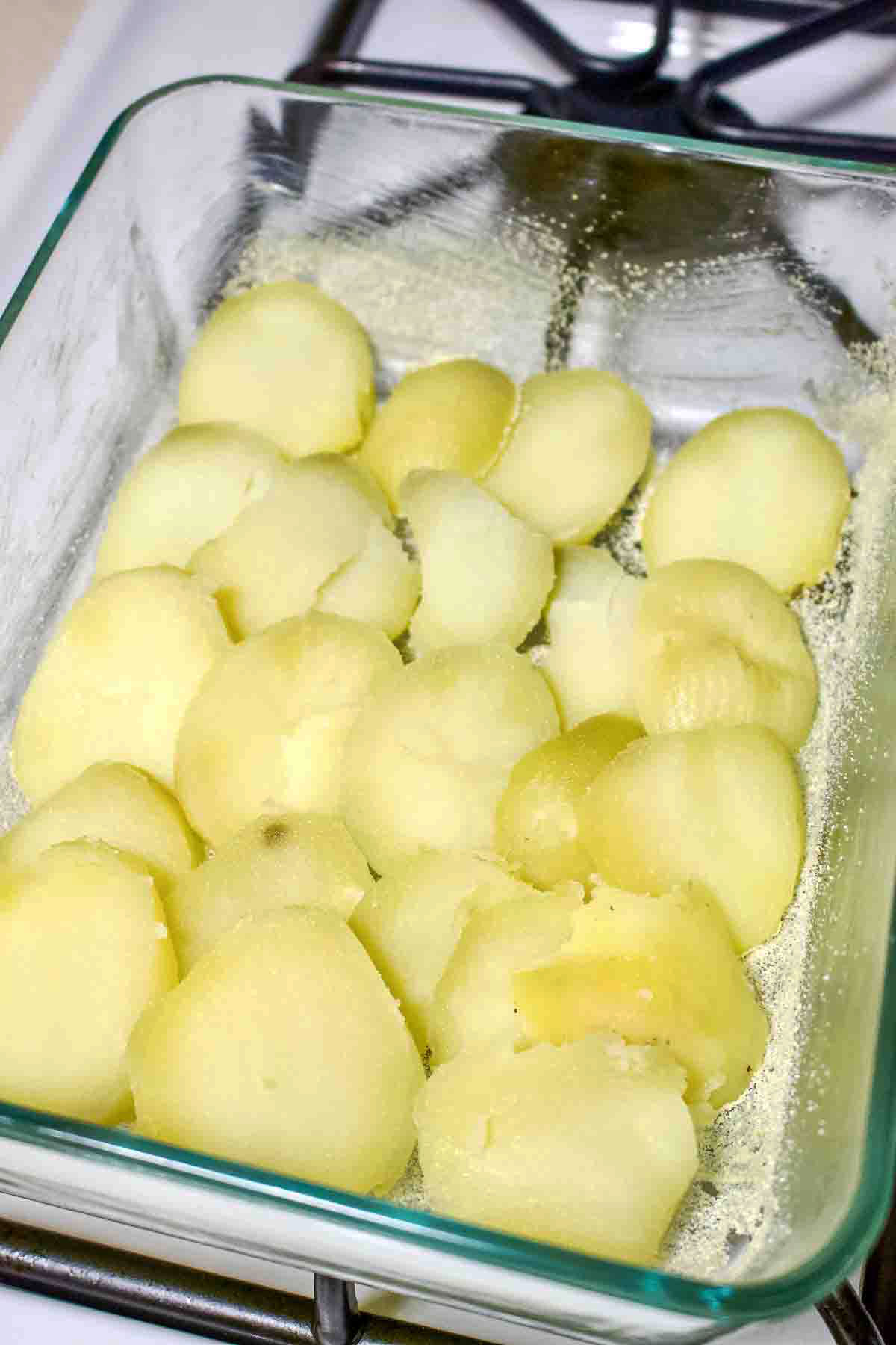 Sliced cooked potatoes on the bottom of a baking pan.