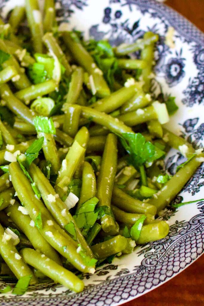 Romanian Garlic Green Beans Salad is a traditional summer salad. An easy way to eat green beans, this salad makes a great addition to your meal. It is served cold and stays well until the next day. In the winter, I use lots of frozen green beans, but in the summer I love going to the Farmers Market and buy fresh ones. Garlic Green Beans Salad in a white and black bowl