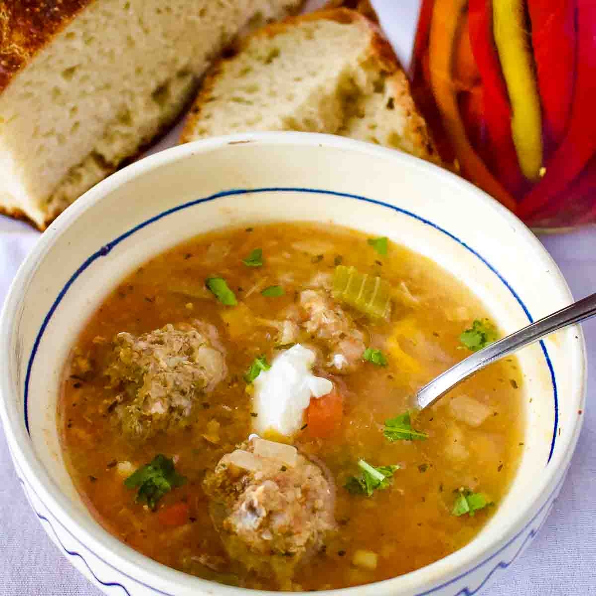 Meatballs Soup in a traditional Romanian bowl served with bread and hot peppers.