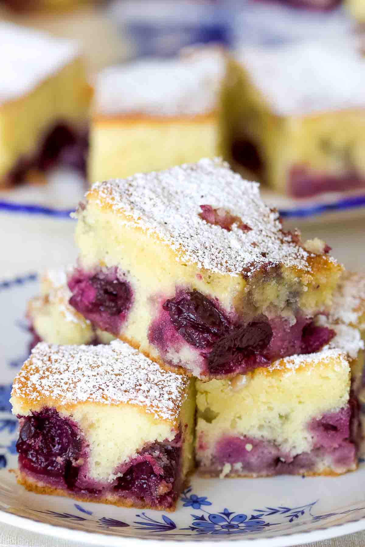 The Pound Cake with Fruits and Almond Flakes is a delicious recipe that can be made all year around using fresh fruits in season or frozen. The cake is not very sweet, but it is delicate and full of flavor. Cherries are the best if you combine them with almonds. Stacked pound cake slices on a white and blue plate.