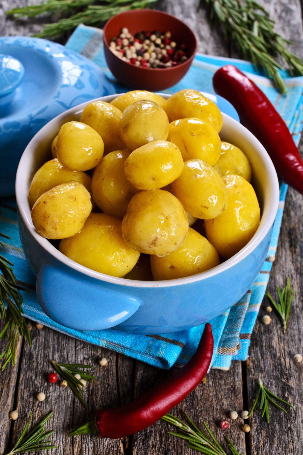 Boiled potatoes in a blue bowl sitting on a blue towel with hot red pepper in the background.