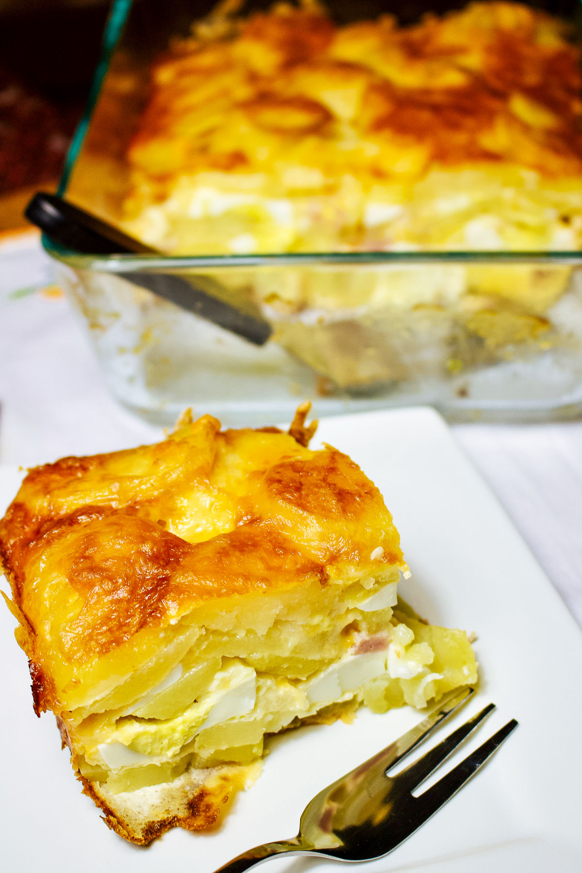 Slice of Potatoes Au Gratin with Ham and Eggs on white plate with fork.