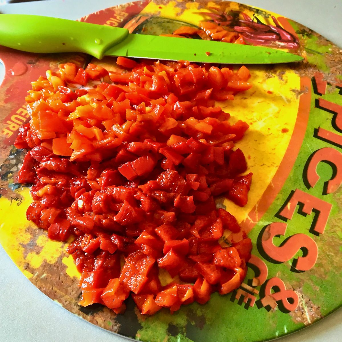 Chopped roasted peppers on a plastic cutting board with green knife.