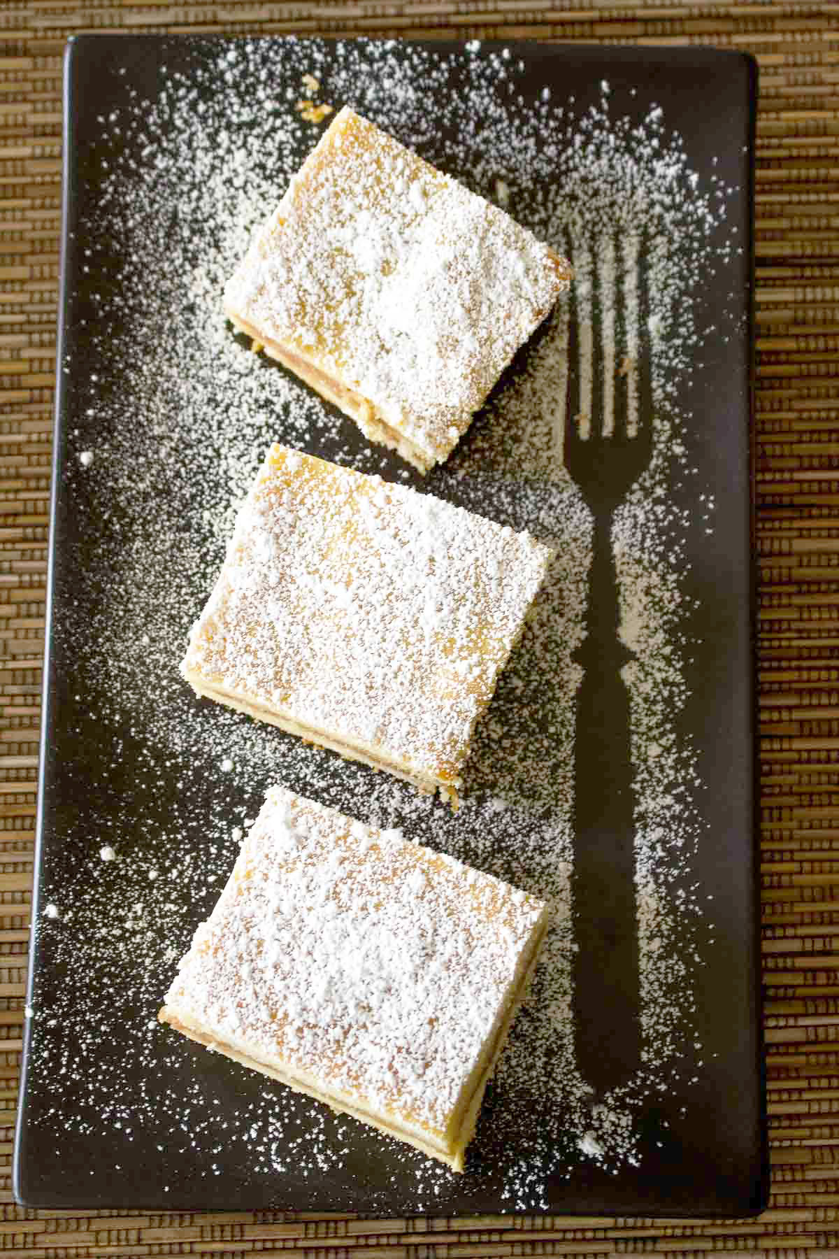Apple Pie Bars on a black platter with powdered sugar.