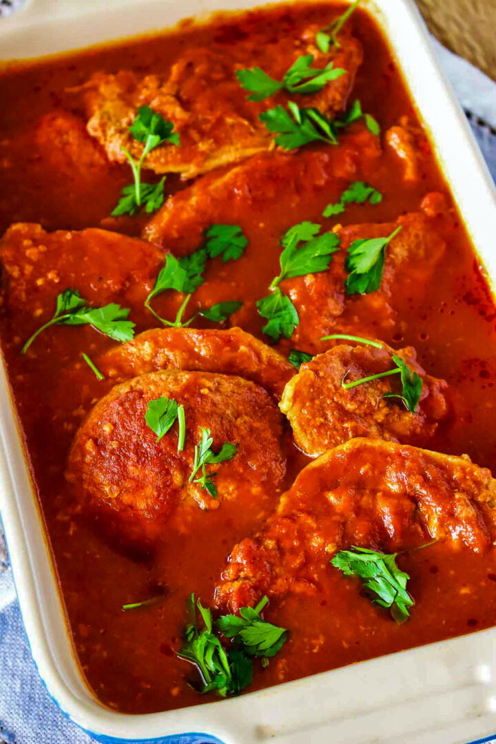 Romanian pork in garlic tomato sauce in a white and blue baking dish.