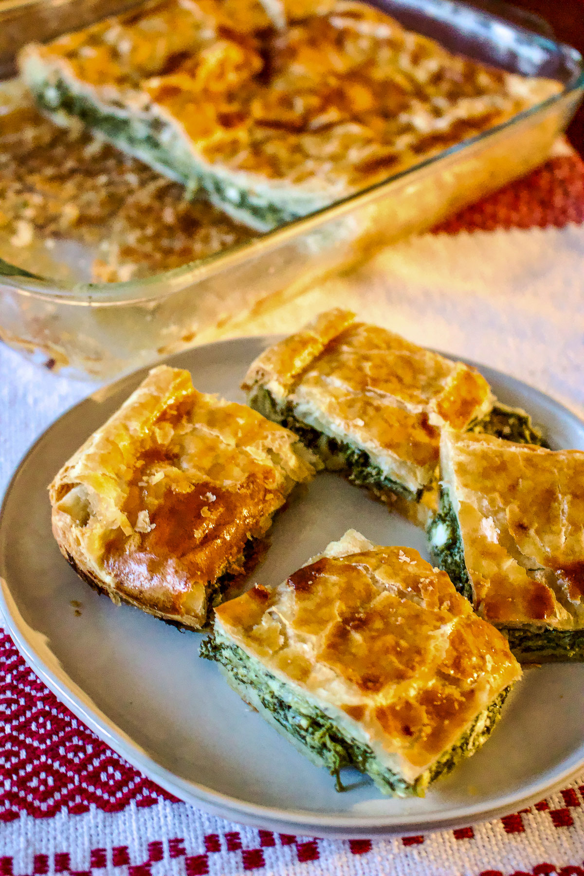 This Romanian Spinach And Feta Cheese Pie is a rustic recipe that is made with puff pastry. A wonderful, relatively easy recipe to make, suitable for vegetarians, this pie is made with spinach, leeks, onions, dill and mint. Slices of Spinach Feta cheese Pie on a white plate0