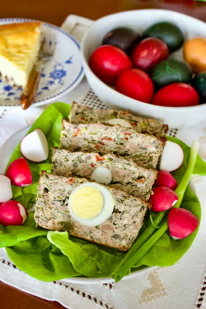 Easter Meatloaf With Hard Boiled Eggs sitting on a platter decorated with lettuce, green onions and radishes.