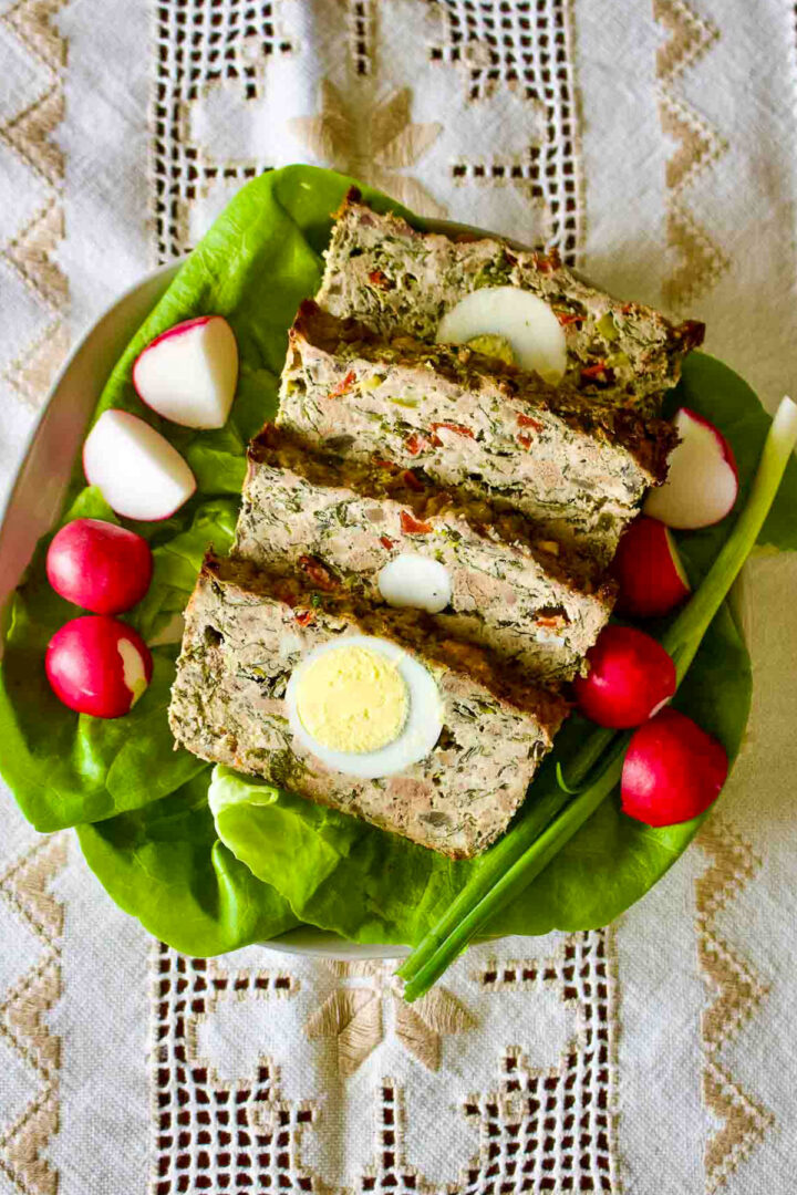 Meatloaf With Hard Boiled Eggs sitting on a platter with lettuce green onions and radishes.