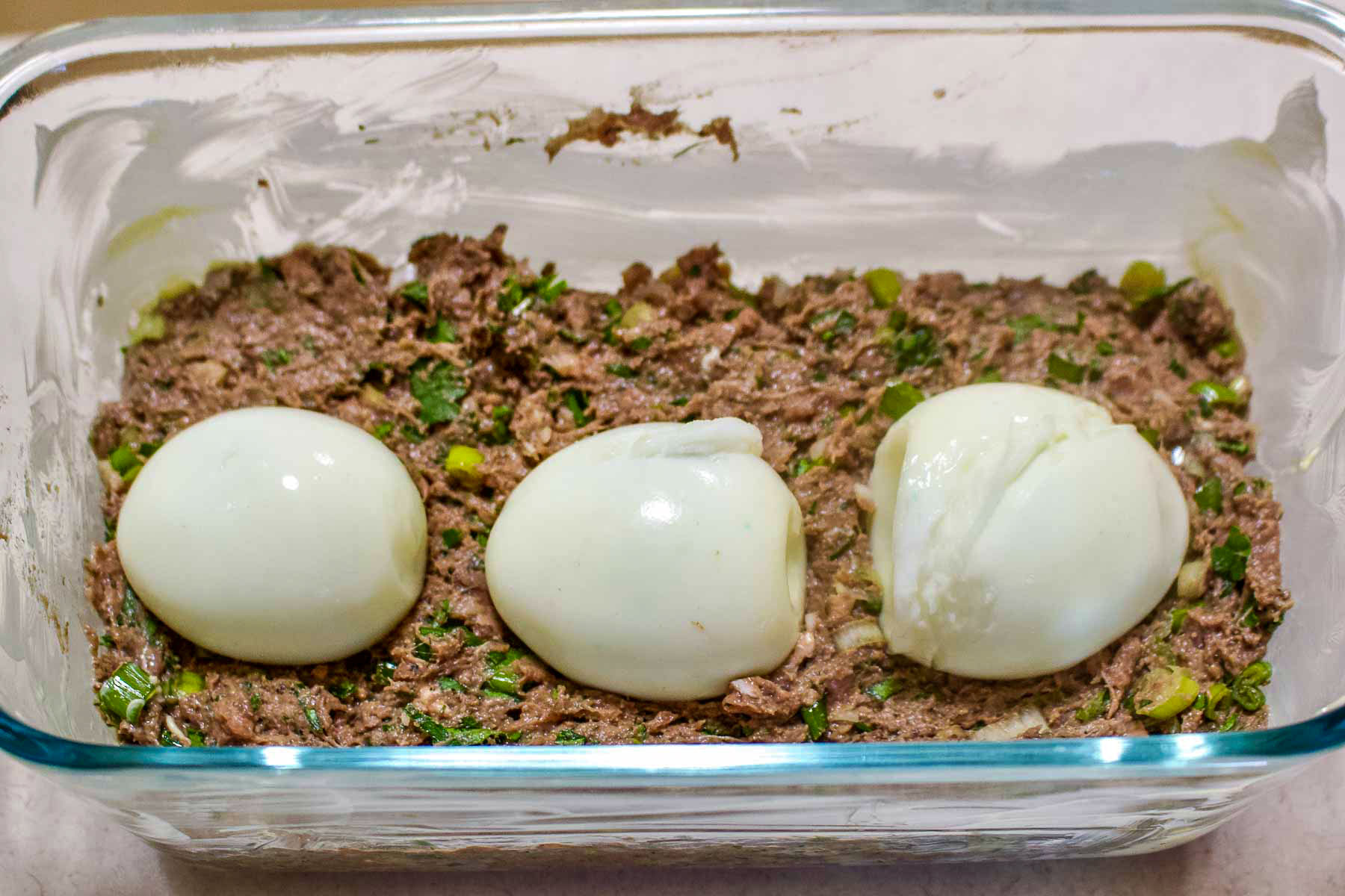 Unbaked meatloaf with hardboiled eggs in a glass baking.