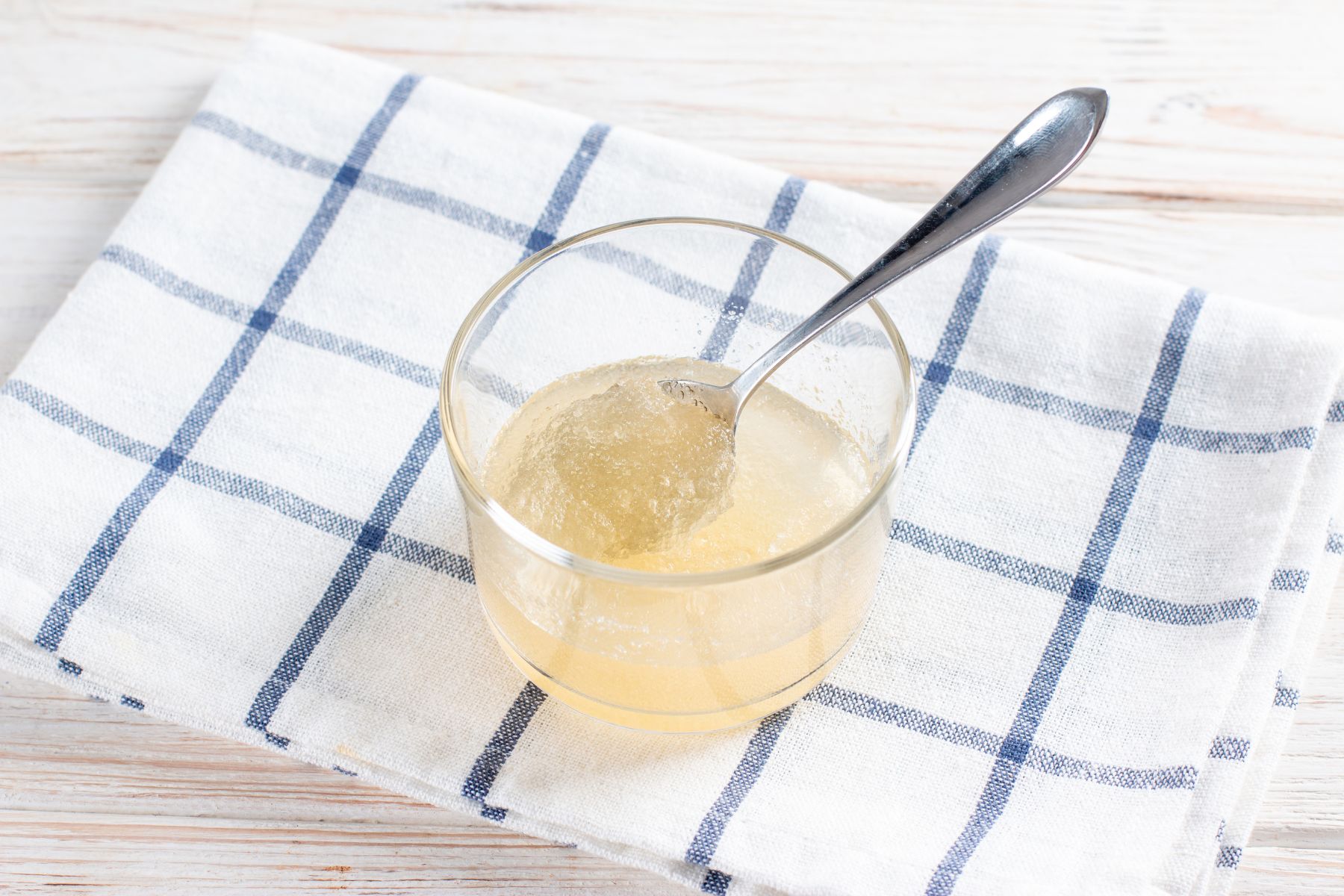 Image showing a small glass with spoon sitting on a tea towel, filled with gelatin blooming in water. 