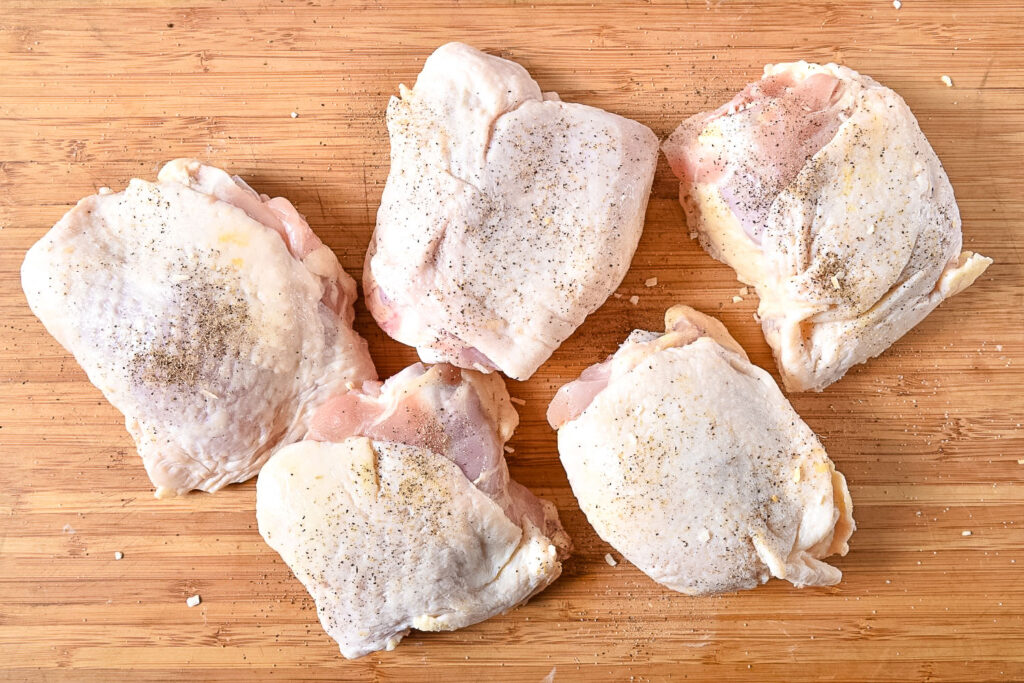 Raw chicken thighs on wooden cutting board0