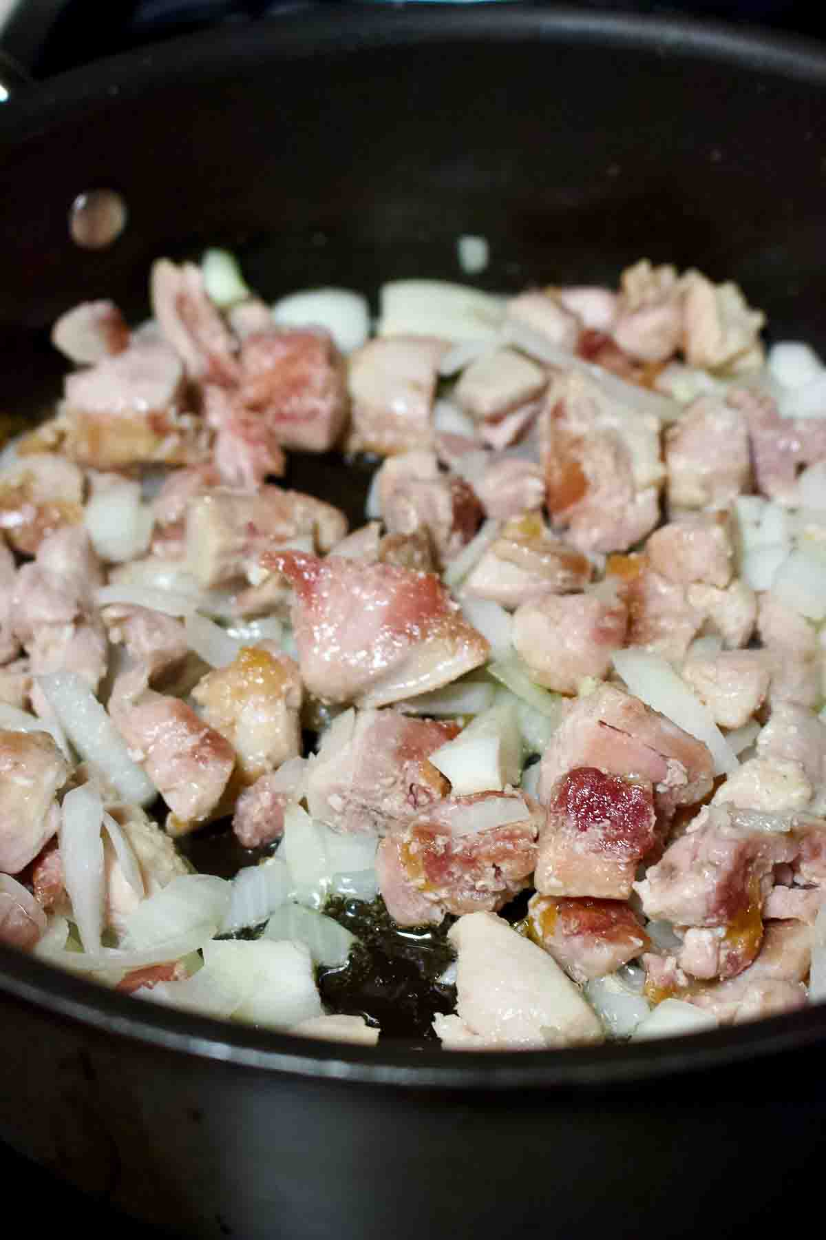 Browned chicken and onions cooking in the pan.