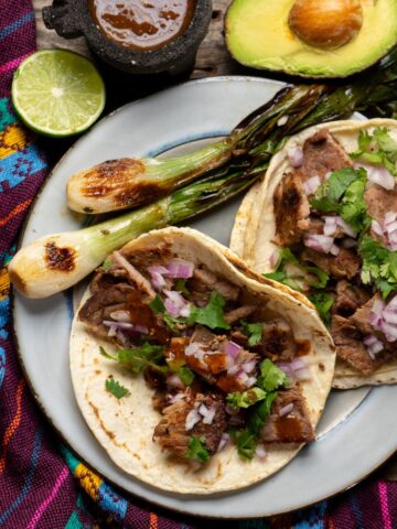 Tacos and grilled onions on a plate with limes and avocado