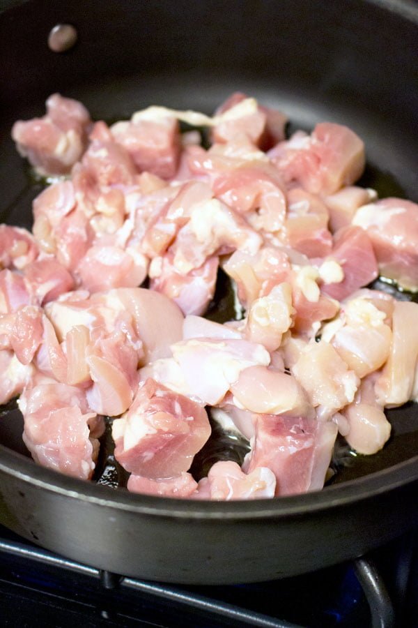 Pieces of raw chicken cooking in a dark pan