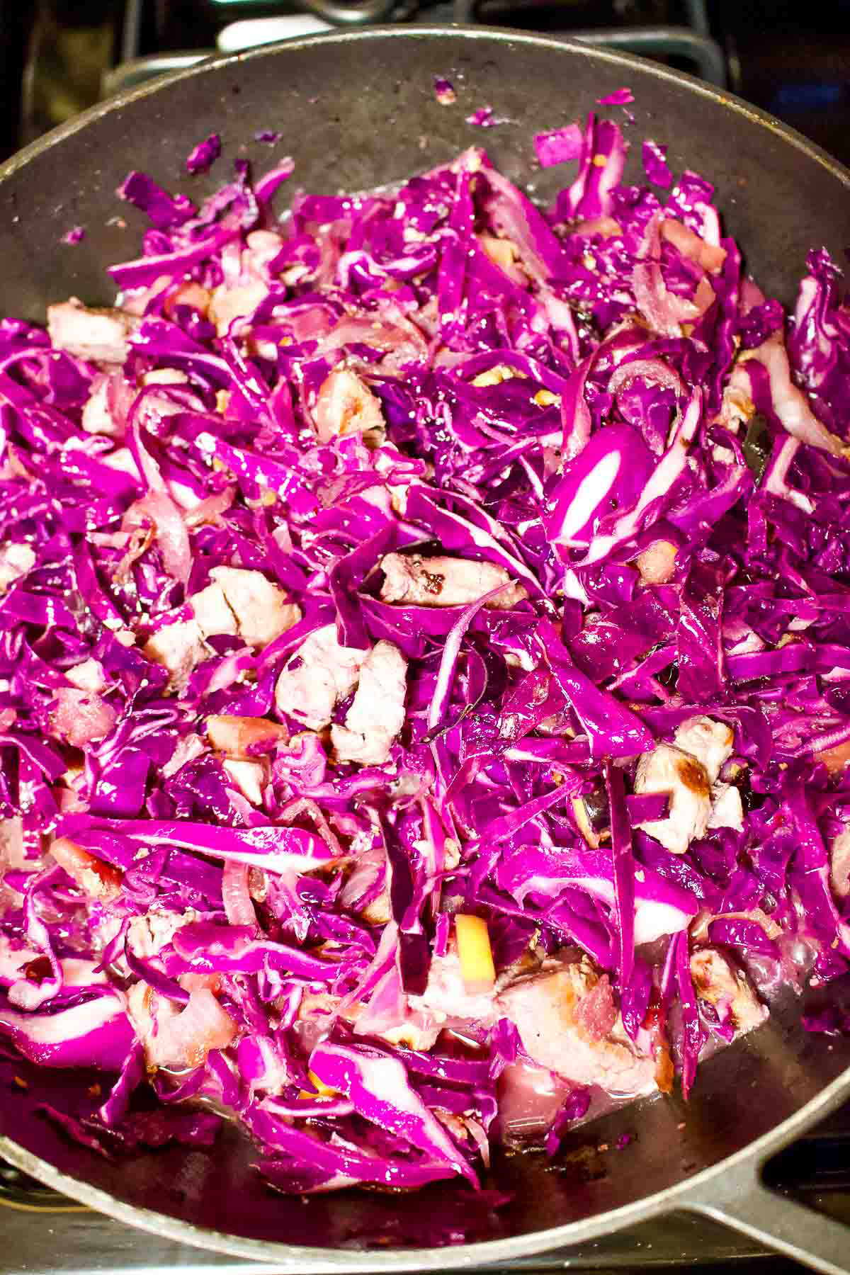 Cooking red cabbage and pork in a skillet.