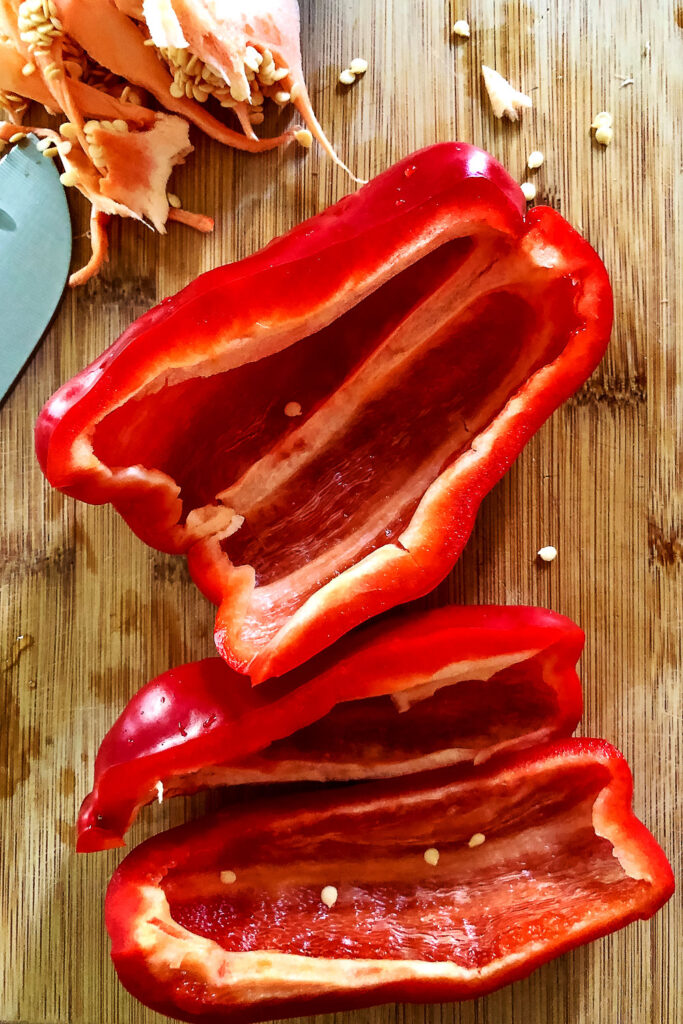 Cored and halved red bell pepper on wooden board