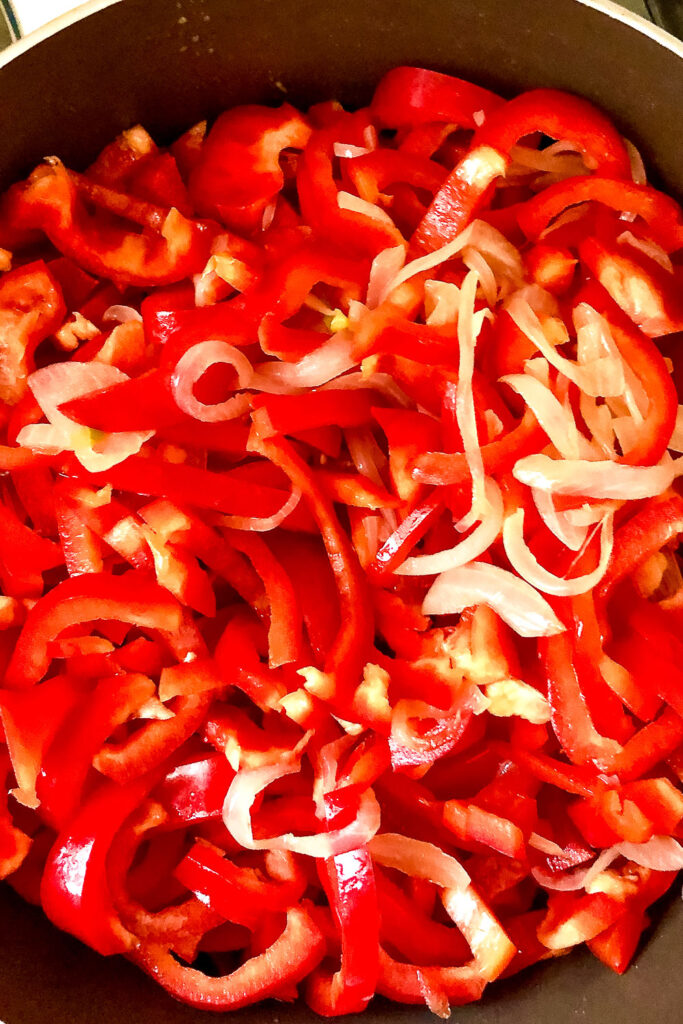 Sliced red peppers cooking with onions in the pan