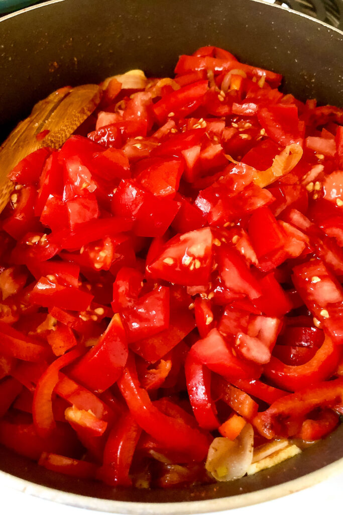 Sliced tomatoes added to Lecso with wooden spoon