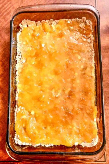 Apricot jam on crust in a baking pan.
