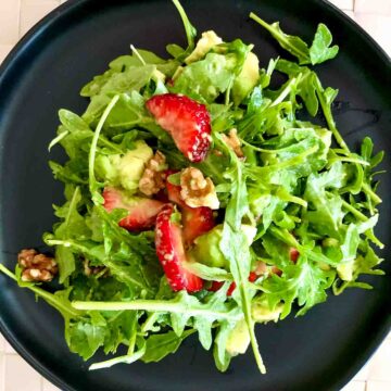 Arugula Strawberry Salad on a black plate.