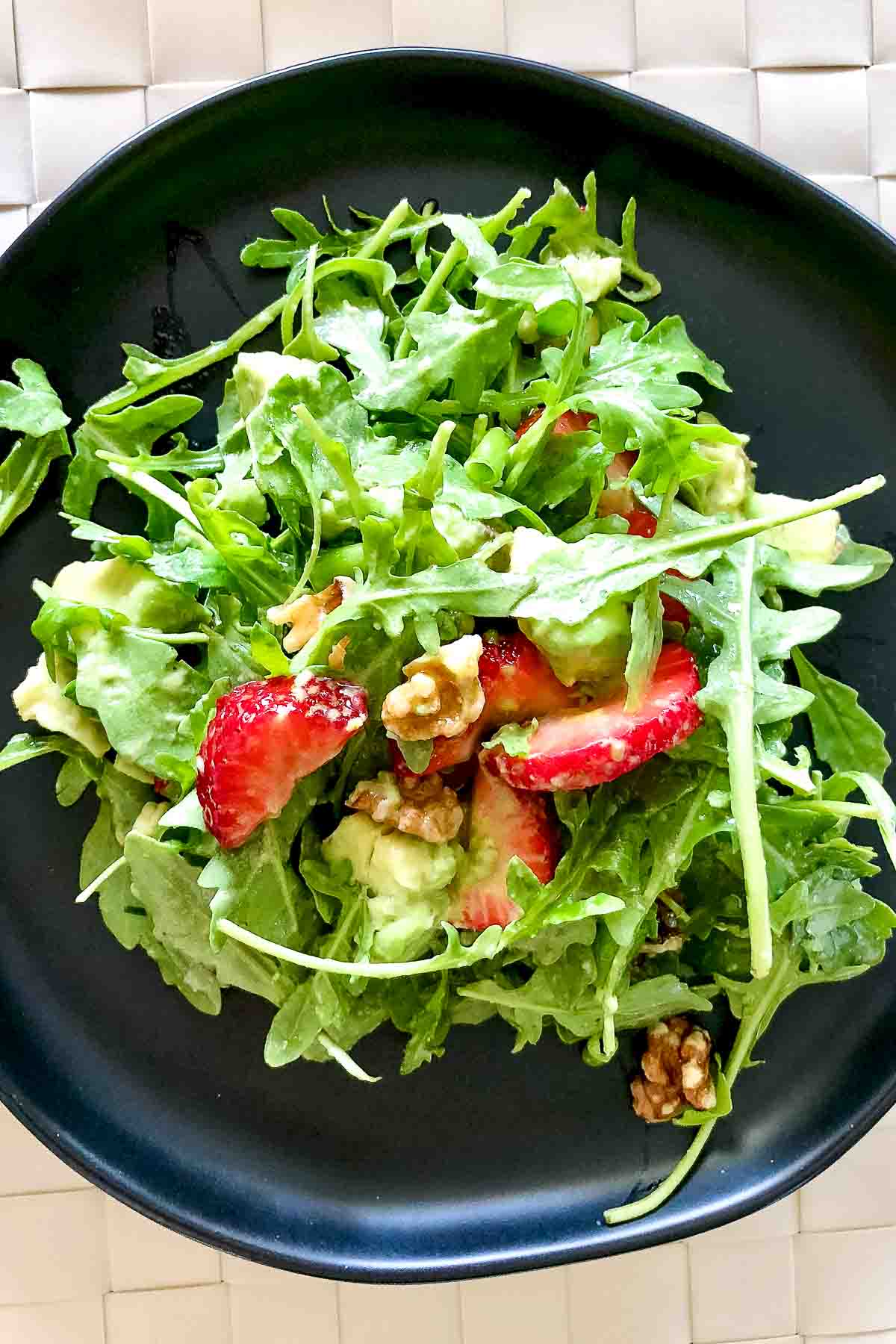 Arugula Strawberry Salad with Pecans and avocado on a black plate.