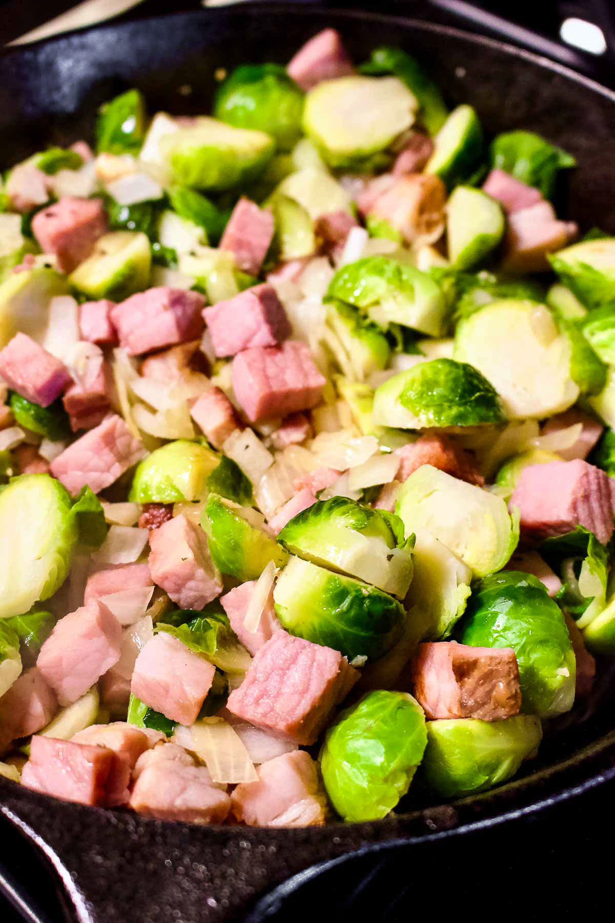 Brussel sprouts cooking in a cast iron with onions and ham.