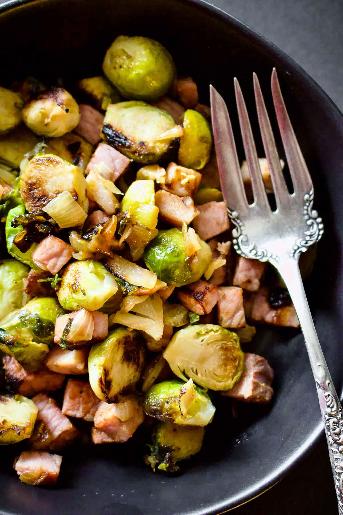 Caramelized Brussel sprouts with ham served in a black serving bowl with decorative fork.