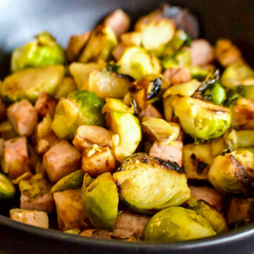 Cast Iron Caramelized Brussel Sprouts With Ham served in a black bowl.