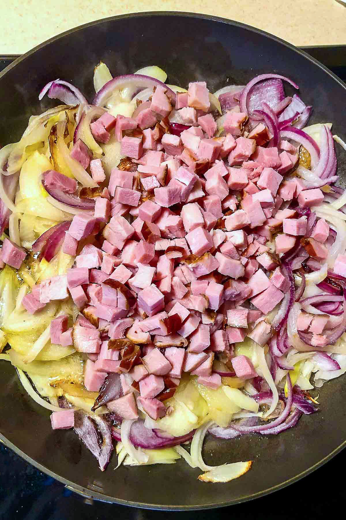 Ham and onions cooking in a skillet.