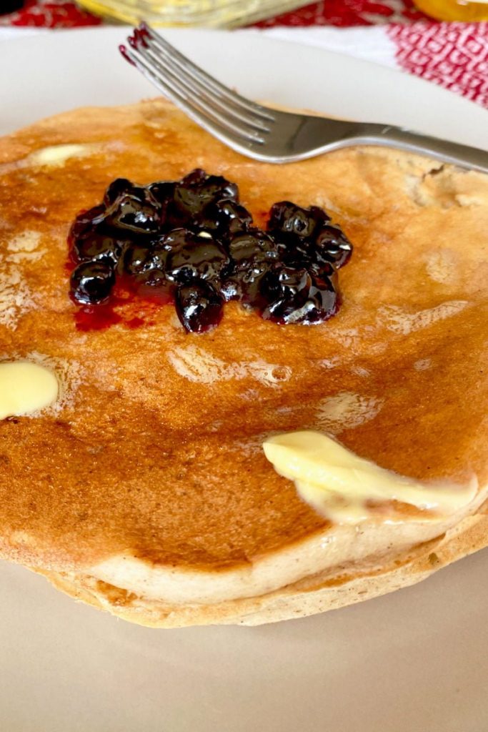 Easy Banana Buttermilk Pancakes with pieces of butter and jam on a white plate and a fork