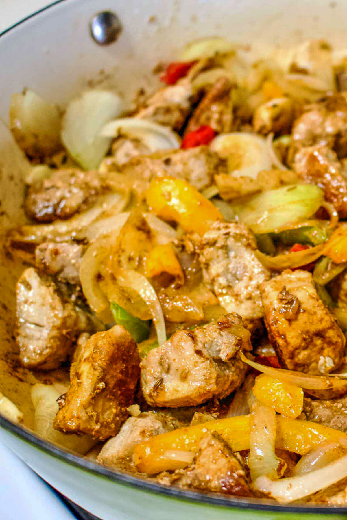 Meat cooking with onions and peppers in a pan.