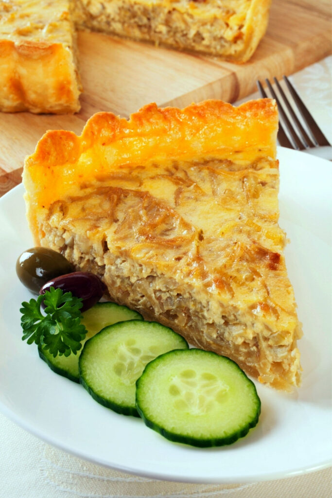 Caramelized onion tart slice on plate with cucumbers and olives0