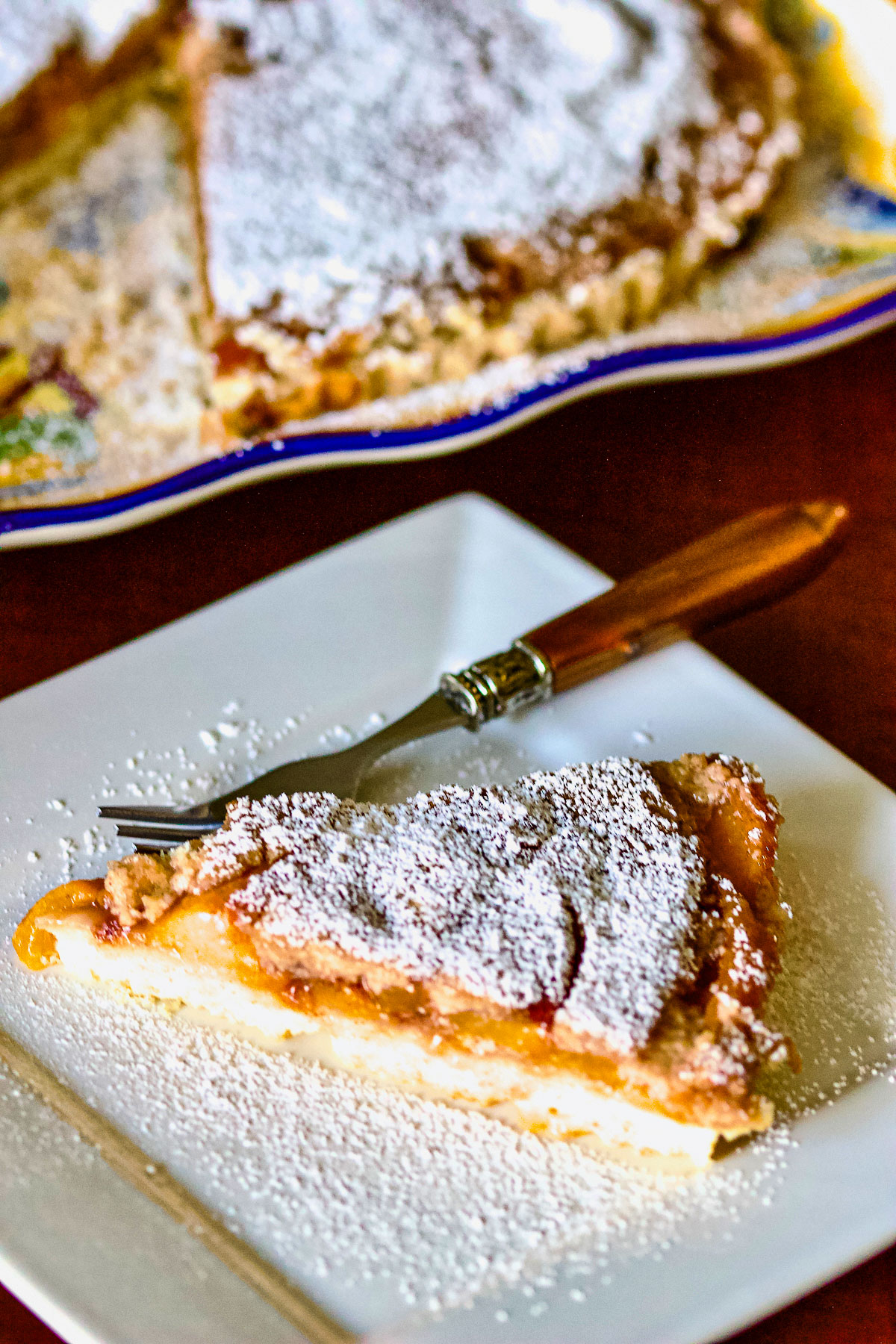 German Peach Kuchen- a Transylvanian dessert made with peaches, custard and a shortbread crust. Delicious, easy to make and perfect for summer. Peach Kuchen slice on a white square plate with fork0