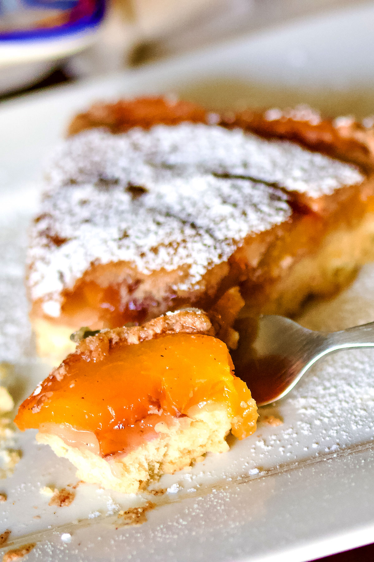 German Peach Kuchen- a Transylvanian dessert made with peaches, custard and a shortbread crust. Delicious, easy to make and perfect for summer. Peach Kuchen slice with fork close up